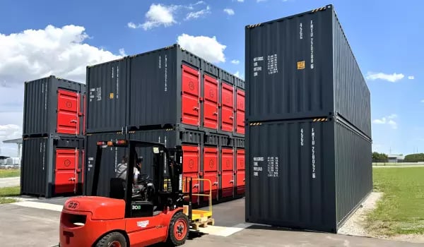 Red and black self-storage shipping containers stacked by a forklift at a FOREMOST modular storage facility, showcasing a 30% cost-efficient storage solution